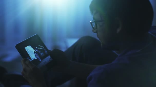 ソファの上の男は、夜のタブレットでアクション映画を見て — ストック動画