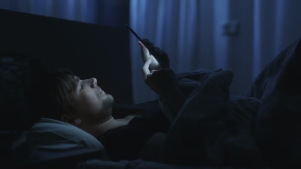 남자는 밤 시간에 집에서 침대에서 태블릿을 사용 하 여. — 비디오