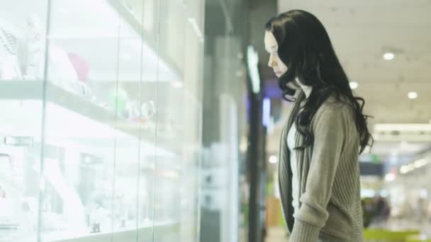 Jeune jolie fille regarde vitrine de magasin de bijoux dans le centre commercial. Tir à la main — Video