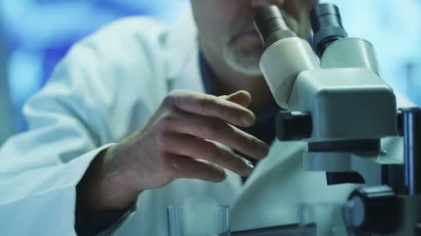Vědec se dívá přes mikroskop a pomocí tabletu v laboratoři — Stock video