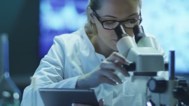 Mujer científica usando microscopio y tableta en laboratorio — Vídeo de stock