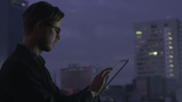 Young Businessman is Using Tablet next to Window at Evening — Stock Video