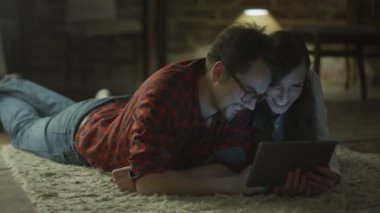 Young Happy Smiling Couple using Tablet PC for Entertainment at Home at Evening Time. Casual Lifestyle.