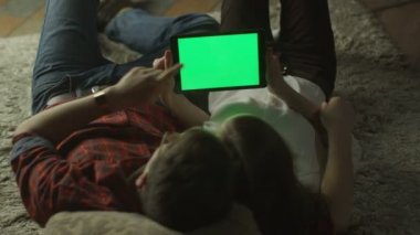 Young Couple are Laying on the floor and Using Tablet PC with Green Screen at Home at Evening Time. Casual Lifestyle.