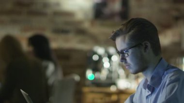 Young Man is Typing on Laptop in Coffee Shop at Evening Time. Casual Lifestyle.