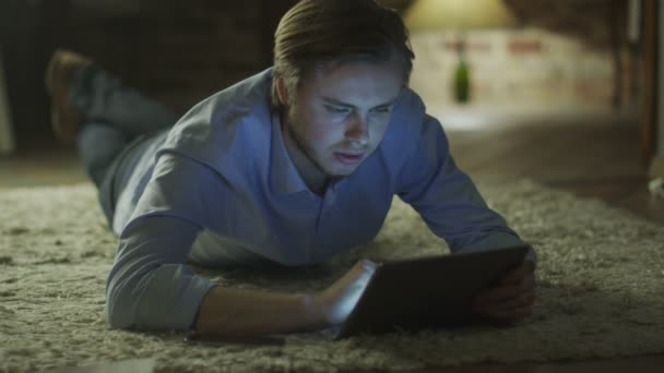 Joven acostado en el suelo y el uso de Tablet PC para el entretenimiento en casa a la hora de la noche. Estilo de vida casual . — Vídeos de Stock