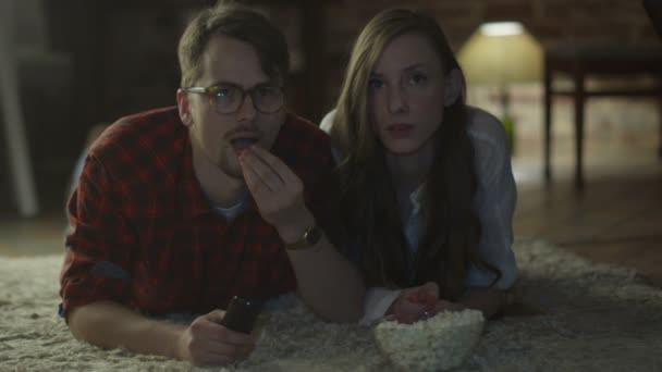 Ein junges Paar liegt auf dem Boden, schaut fern und isst abends zu Hause Popcorn. Casual Lifestyle — Stockvideo