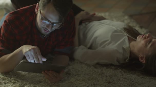 Casal jovem estão deitados no chão e relaxante à noite em casa usando Tablet PC. Estilo de vida casual — Vídeo de Stock
