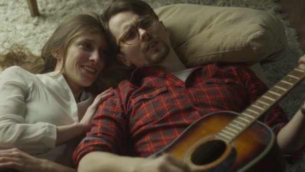 Young Happy Smiling Couple are Laying on the Floor and Playing Guitar at Evening Time at Home. Casual Lifestyle. — Wideo stockowe