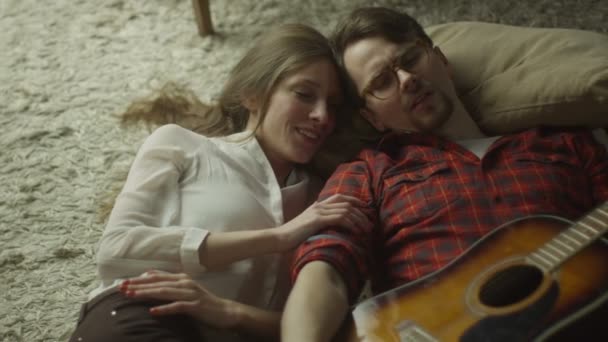 Ein fröhlich lächelndes junges Paar liegt auf dem Boden und spielt abends zu Hause Gitarre. Casual Lifestyle. — Stockvideo