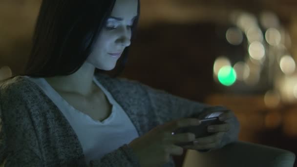 Chica adolescente con hermosa sonrisa está utilizando el teléfono inteligente en la noche. Estilo de vida casual . — Vídeo de stock