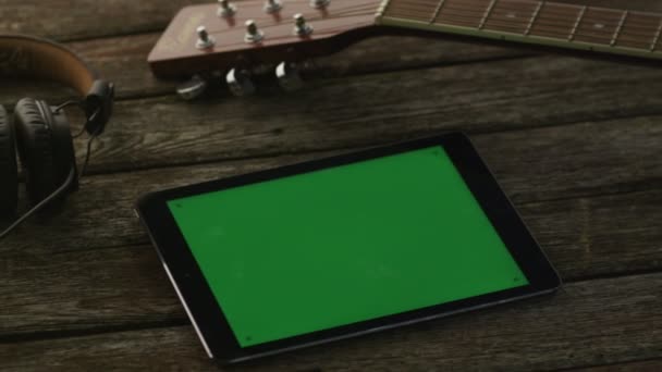 Tablet PC com tela verde Deitado em mesa de madeira ao lado de guitarra e fones de ouvido. Estilo de vida causal — Vídeo de Stock