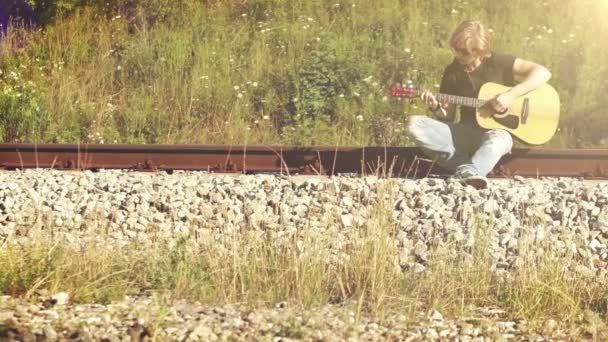 Молодой человек, играл на гитаре на железной дороге — стоковое видео