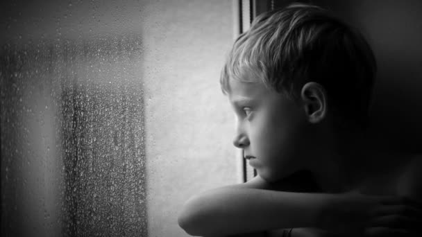 Allein kleiner Junge schaut Regentropfen durch Fensterglas — Stockvideo