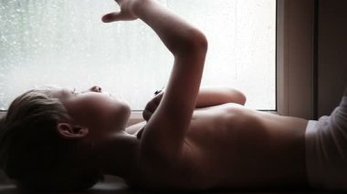 Yağmur damlaları cam pencere üzerinde üzgün çocuk izliyor
