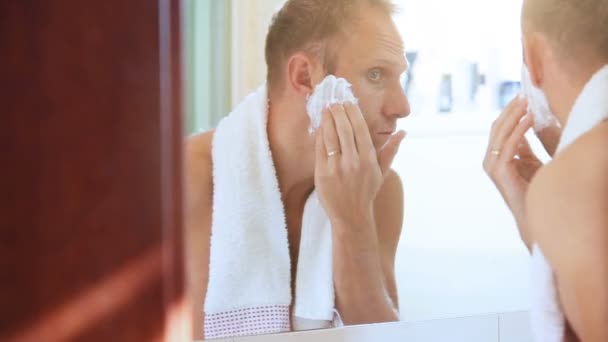 Morning regular bathroom scene: young adult man foames his face before shaving — Stock Video