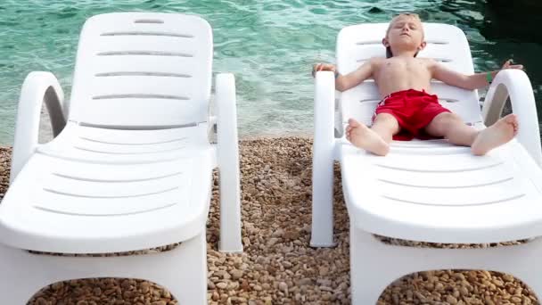 Mały chłopiec opala na wybrzeżu Morza w biały leżak — Wideo stockowe