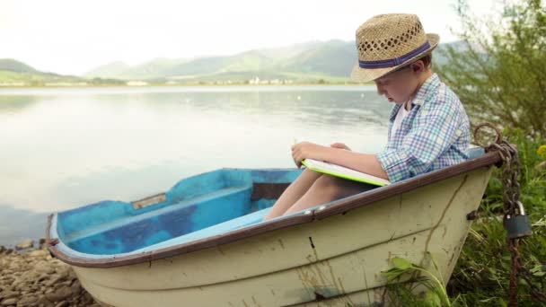 Menino lendo um livro interessante no velho barco — Vídeo de Stock