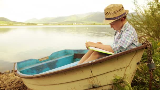 Boy sitting in an old moored boat reading a book — Stock Video