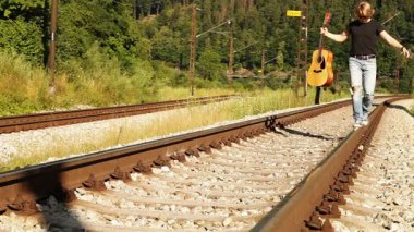 Merry teenager balancing with guitar on the railways dressed ripped denim walk on the railway