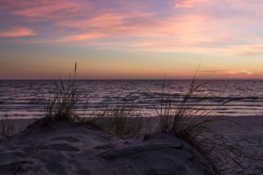 Kum tepelerinde büyüyen çimenler ve arka planda güzel bir günbatımı görülebilir. Sığ alan derinliği yumuşak, rüya gibi bir ruh hali vermek için kullanılır.