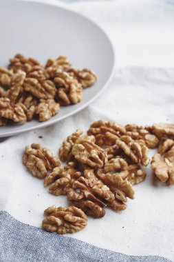 Beyaz mavi masa örtüsü, el işi kağıt ve gri yuvarlak tabakta ceviz çekirdekleri. Vejeteryanlar için olgun ceviz meyvesi