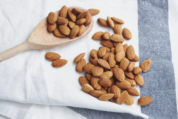 Almond kernels on white fabric. A handful of nuts on the tablecloth. Food for vegans, ingredients for making almond milk. with a wooden spoon on the background