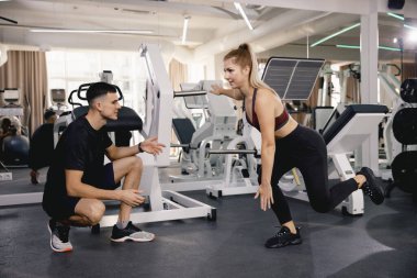 Koç spor salonundaki ayak egzersizinin doğruluğunu kontrol eder. Spor salonunda antrenman küçük bir gruptur. Bir erkek ve bir kız birlikte antrenman yapıyor..