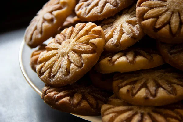 Siyah bulanık arkaplanda cam bir tabakta pudra şeker ve kakaolu kurabiyeler.