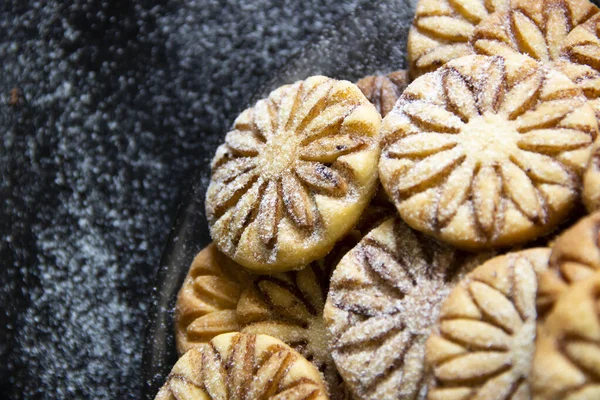 Siyah bulanık arkaplanda cam bir tabakta pudra şeker ve kakaolu kurabiyeler.