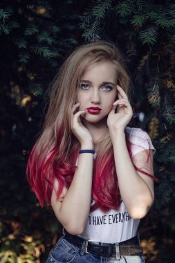 Yüzü yeşil bitkilerin gölgesinde, mavi gözlü genç sarışın kızın yakın portresi.