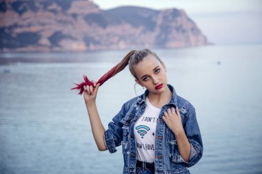 Parlak gözlü ve dudaklı genç bir kız. Şık bir saç stili ve mavi denize karşı duran bir görüntüsü olan bir sarışın. Arkaplan sanatsal açıdan bulanık