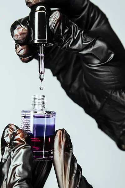 Cosmetic oil for salon procedures. A drop of product is visible on the oil dispenser. Hands in black gloves hold nail and cuticle care product.