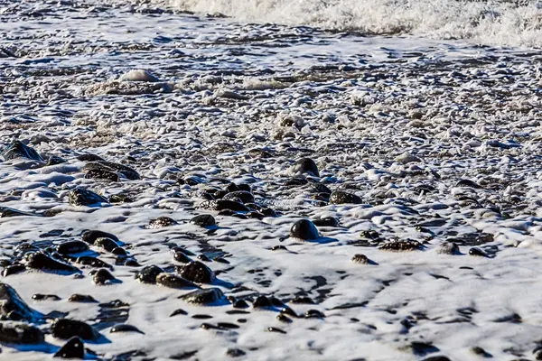 Stenen in schuim op het strand — Stockfoto