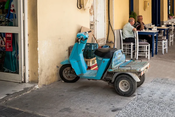 : La motocicleta de carga permanece estacionada cerca de la tienda mientras el conductor está sentado en la cafetería en la ciudad de Paleochora — Foto de Stock