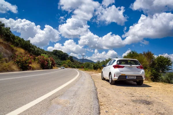 Beyaz Toyota Auris Crete adasının yolda bulutlar arasında park edilmiş kalır. Toyota Auris kompakt hatchback olduğunu