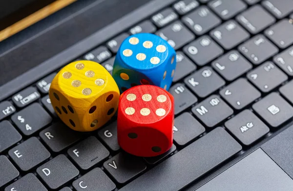 Three colorful wooden game dice showing six laying on a modern laptop keyboard. Lots of dice showing six, winning, lucky number, great odds and good throw simple abstract concept