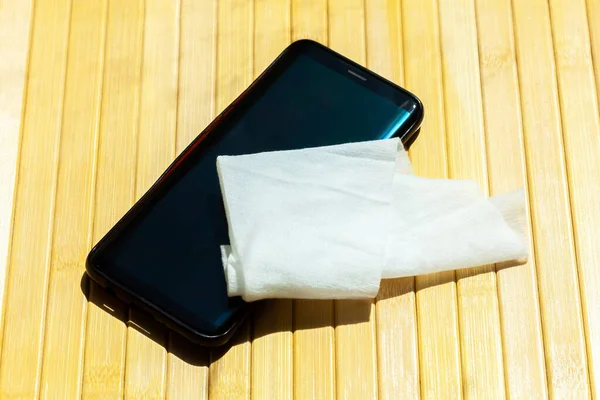 Modern smartphone and a wet wipe, damp tissue on the table Mobile phone disinfecting, cleaning, sanitizing, technology and hygiene during covid 19 pandemic abstract concept. Health care good practices