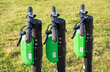 Dışarıya park edilmiş üç tane elektrikli scooter, parmaklıklar, nesne detayları, yakın çekim, kimse yok. Şehir ulaşımı, halka açık kiralık elektrikli araçlar, şehir hayatı