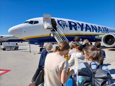 Havaalanı önlüğü üzerinde yolcu kuyruğunda bekleyen yolcular Ryanair Boeing 737 'ye doğru yürüyor açık kapılı güneşli mavi gökyüzü seferi sahnesi düşük maliyetli havayolu biniş süreci, el bagajları ve sırt çantaları