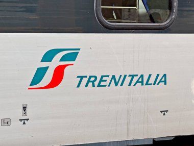 Trenitalia logosu ve adı pencereli, beyaz metal gövdeli, mavi çizgili, Avrupa 'da demiryolu taşımacılığı markalı bir İtalyan yolcu vagonunun yanında.
