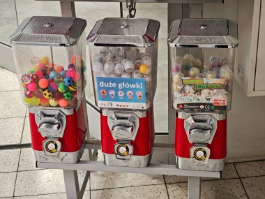 Arka arkaya renkli lastik topları ve plastik sürpriz kapsülleri olan üç adet bozuk para işleten kapsül oyuncak otomatı, alışveriş merkezinin girişinde kırmızı retro sakız makineleri, insan yok, çocukluk ödülleri.