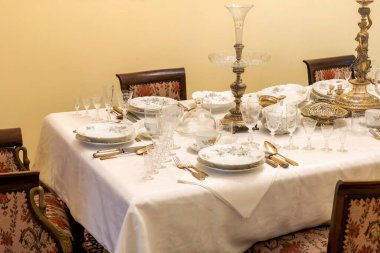 Beyaz masa örtüsü, çiçekli porselen tabaklar, kristal cam eşyalar ve süslü şamdanlar, boş yemek yok insan yok, klasik iç mekan.