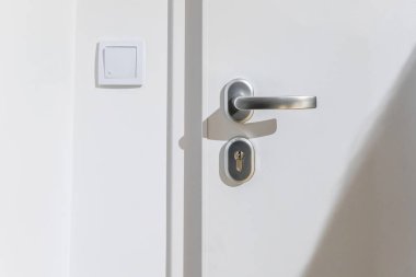 Modern beyaz apartman giriş kapısı gümüş kollu anahtar deliği, ön görüş minimal ışık anahtarı, güneş ışığı fotokopi alanı, ev güvenliği kiralama konsepti, insan yok.