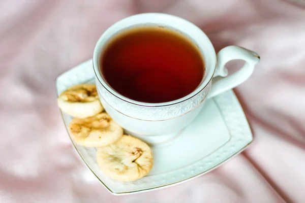 絹のテーブルクロスに乾燥した日付のデザートの横に ソーサー付きのお茶と白のカップ — ストック写真