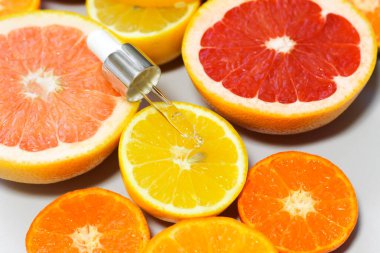 Beyaz arka planda farklı narenciye meyveli C vitamini içeren yüz serumu..