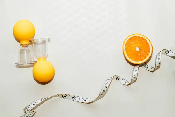 Vacuum massage anti-cellulite cups on a gray background with an orange and centimeter. Self-massage for healthy skin.