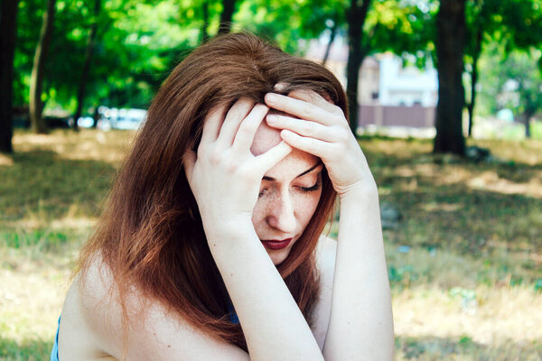 A young pretty girl with red hair is holding her head, it became bad on the street, very sad.