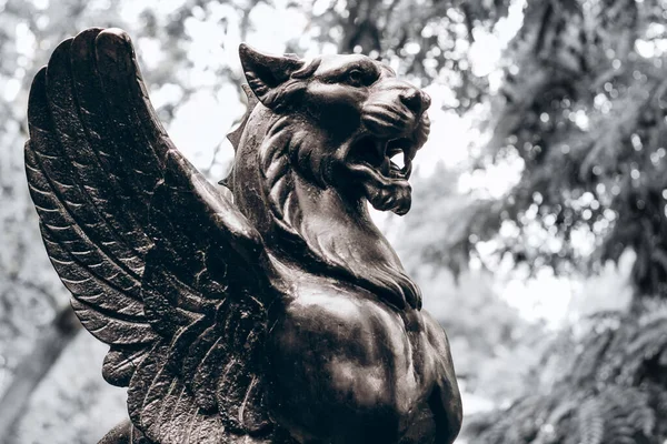 antique dark sculpture of a lion with wings on a colorless background.