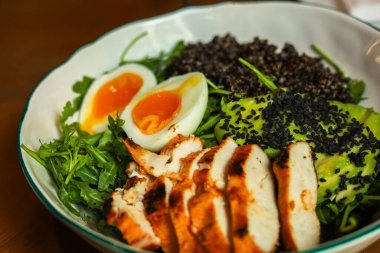 Lezzetli bir salatada ızgara tavuk, canlı sebze bıldırcın yumurtası ve siyah pirinç bulunur. Tabak, taze malzemeler ve renkli bir görünüm içeren bir kasede düzenleniyor..